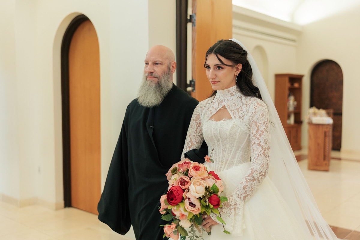 A priest escorts the bride into the nave