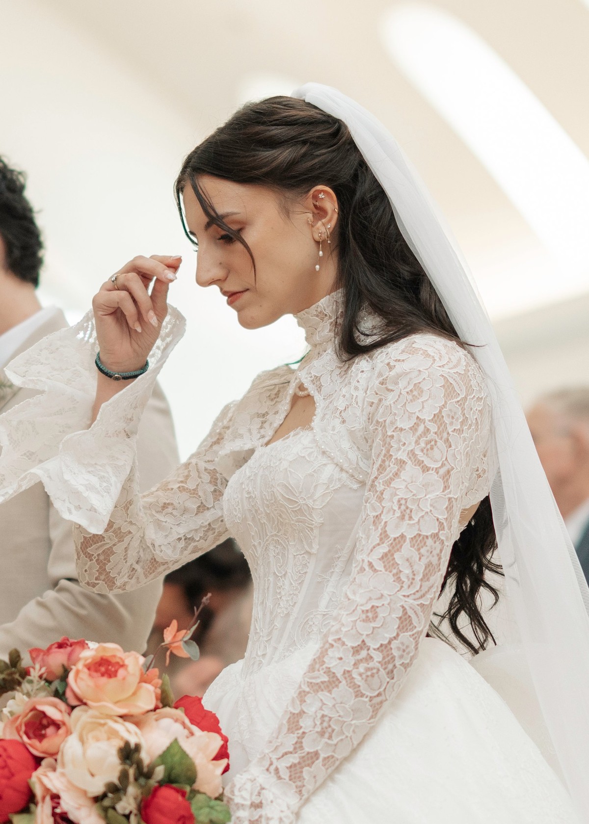 The bride makes the sign of the cross while holding her bouquet