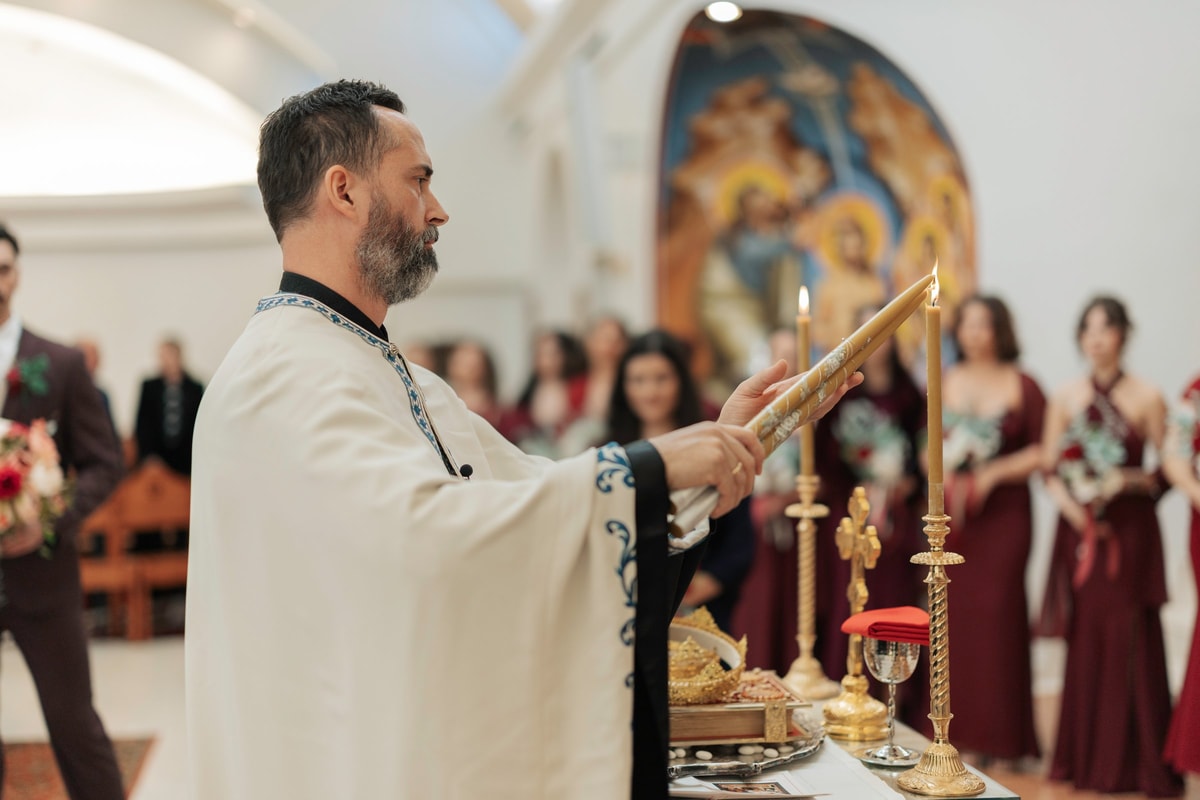 A priest raises a hand cross beside the wedding candles