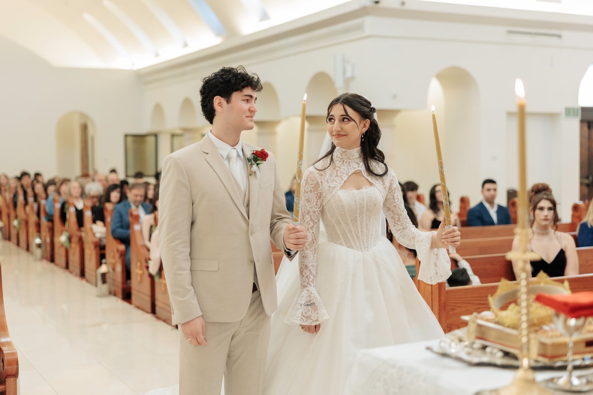 The bride and groom stand together holding candles during the service