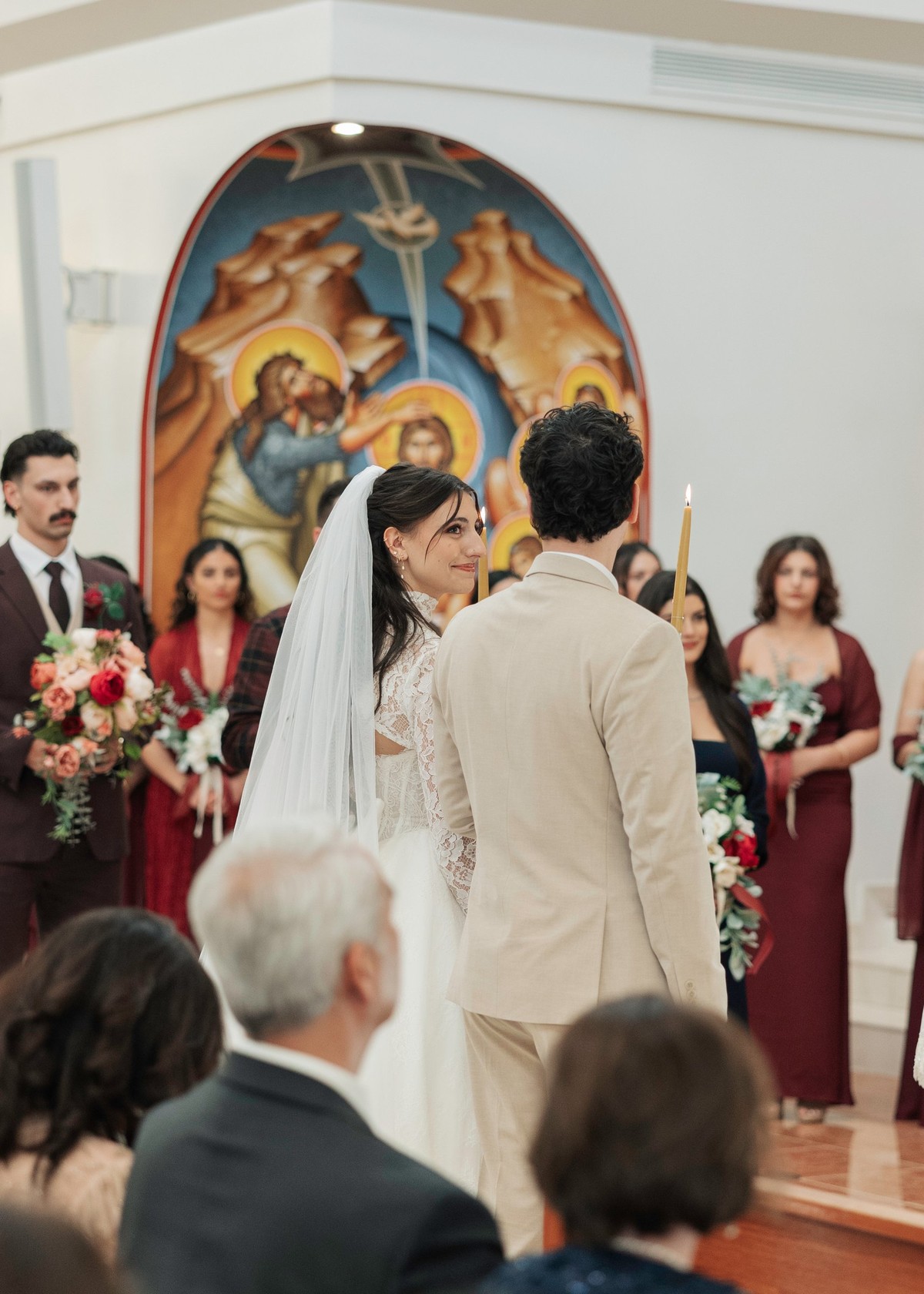 The bride and groom stand together holding candles during the service