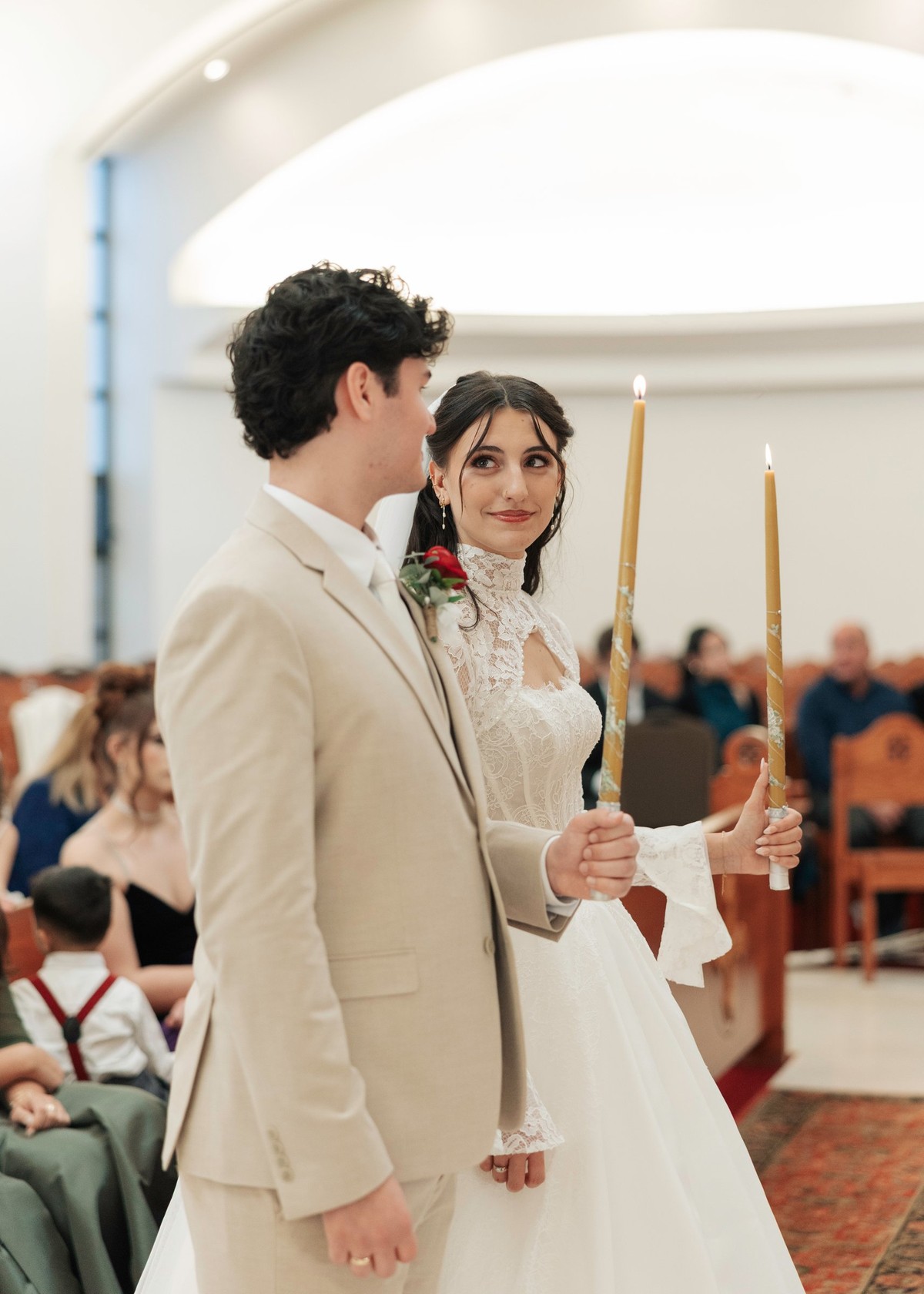 The bride and groom stand together holding candles during the service