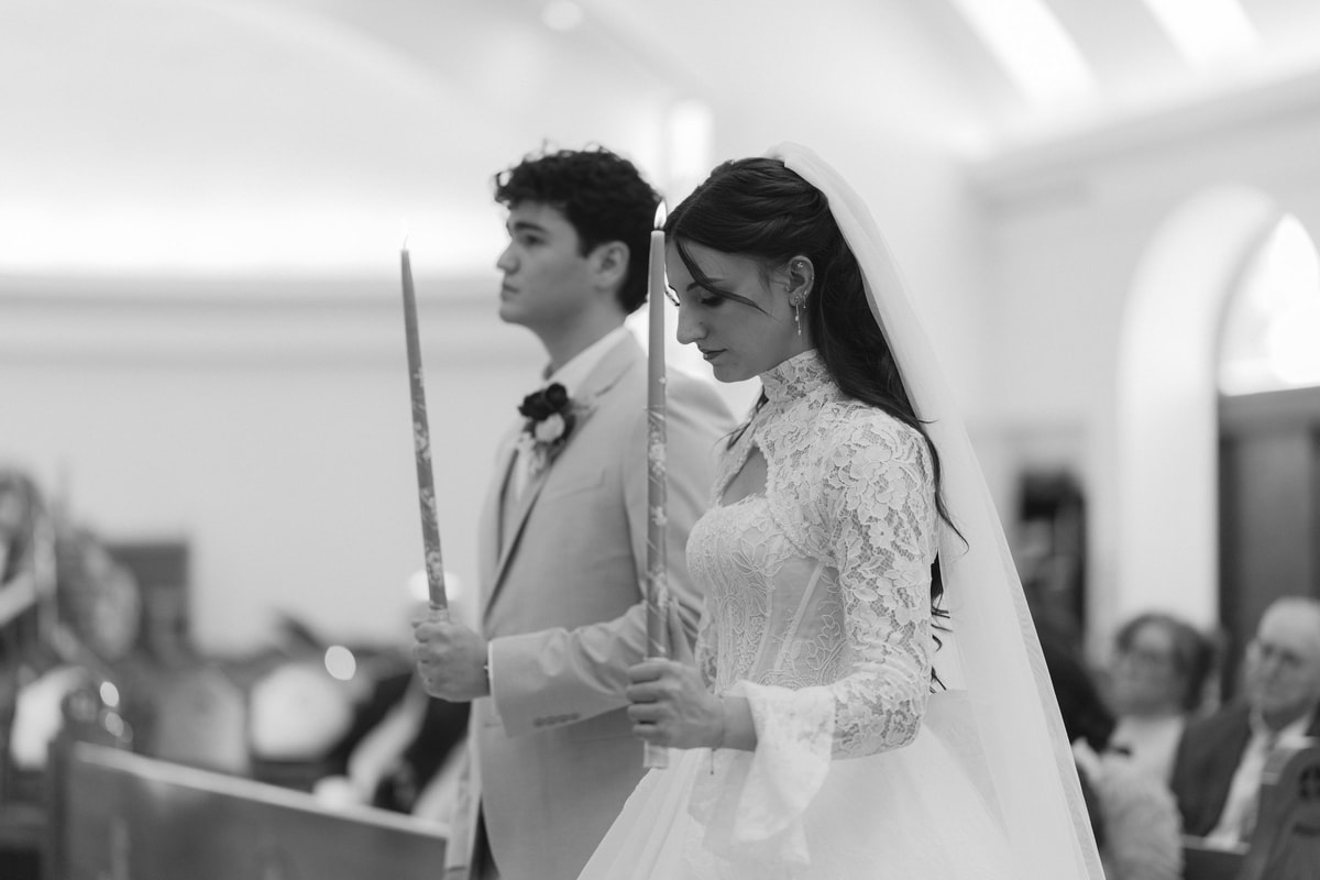 The bride and groom stand together holding candles during the service
