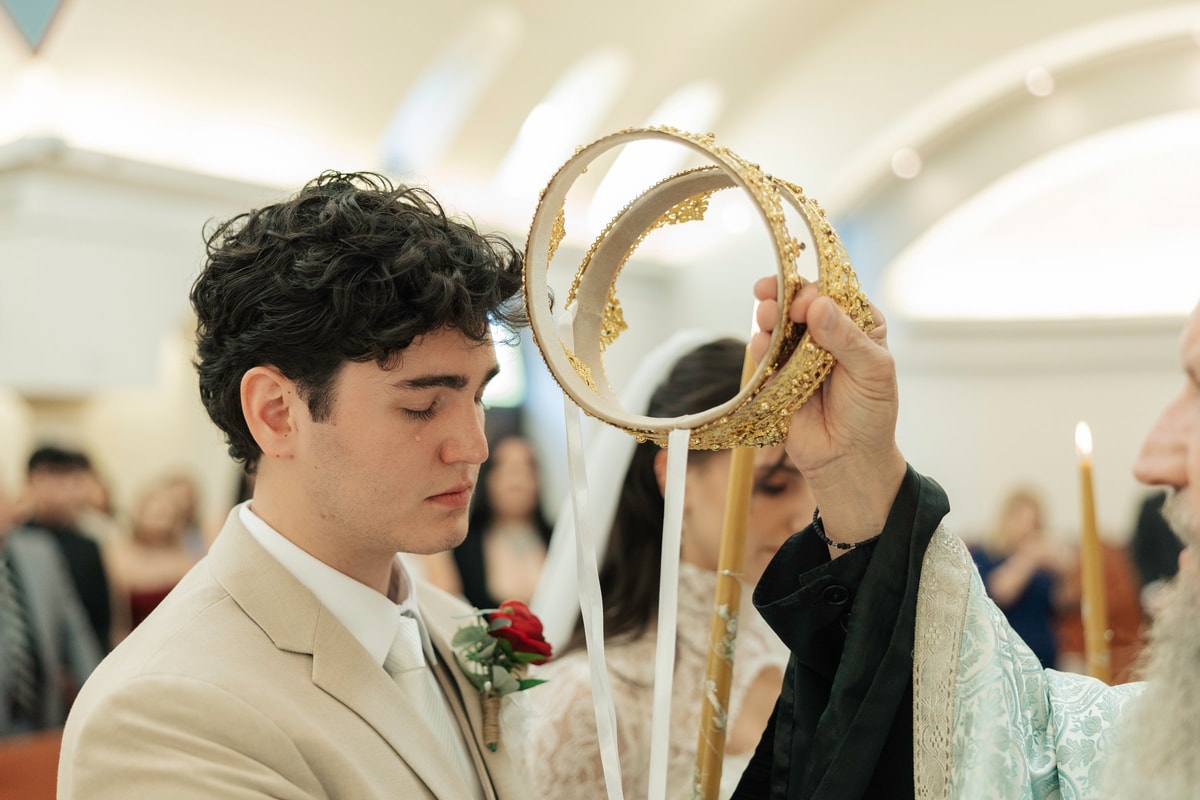 An Orthodox priest holds an ornate wedding crown above the groom