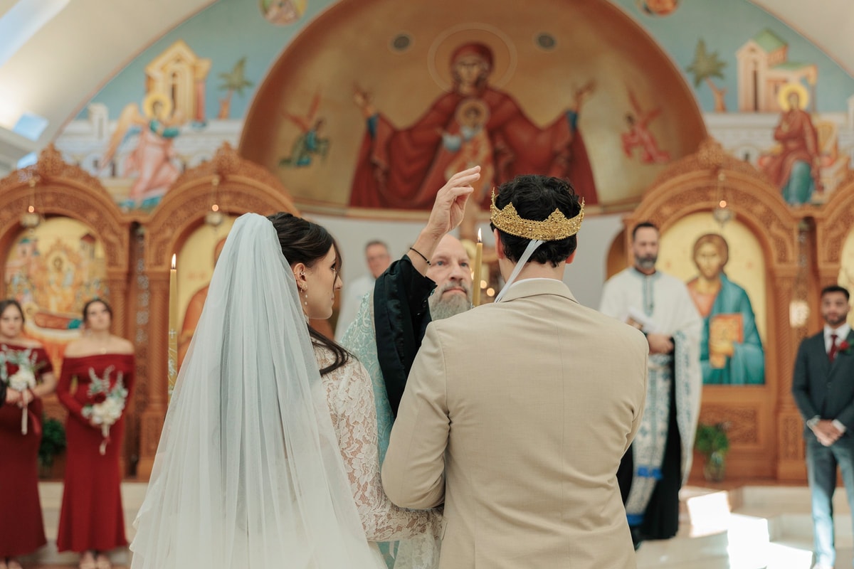 The bride and groom stand crowned before the iconostasis