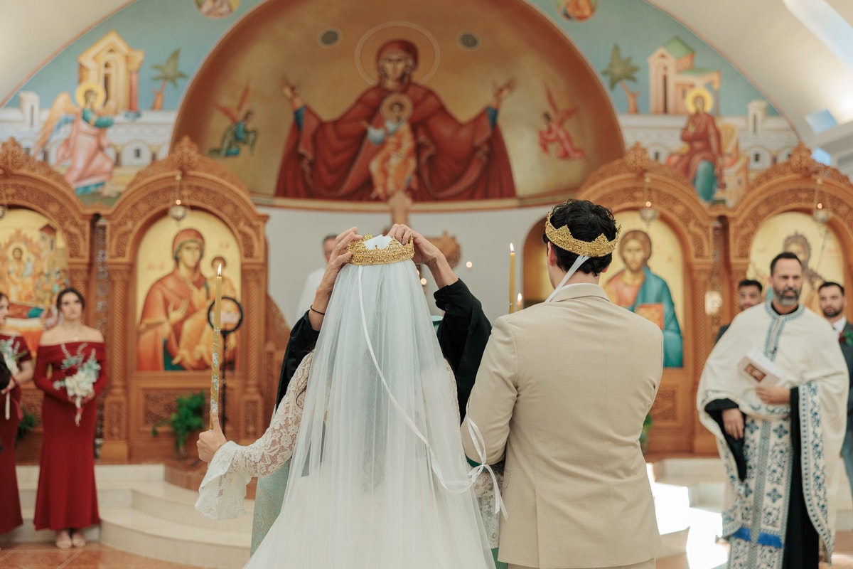 The bride and groom stand crowned before the iconostasis