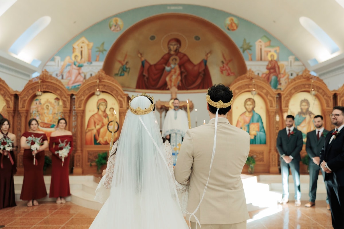 The bride and groom face the iconostasis wearing their wedding crowns