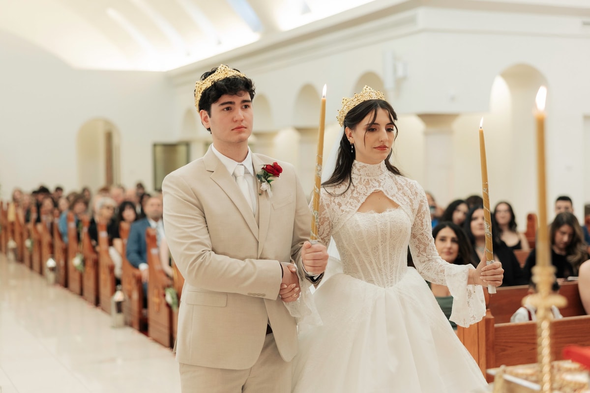 The crowned couple walks together holding candles