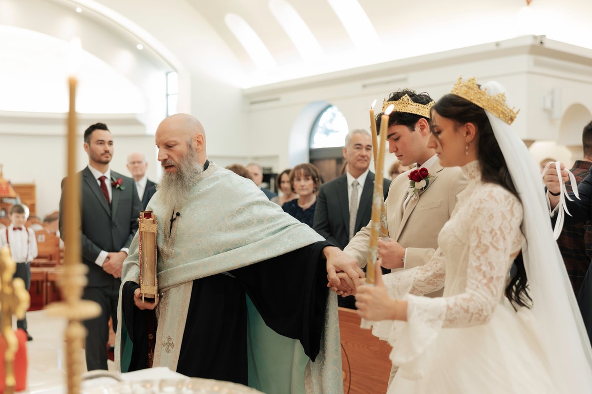 An Orthodox priest stands before the crowned bride and groom with his vestment extended