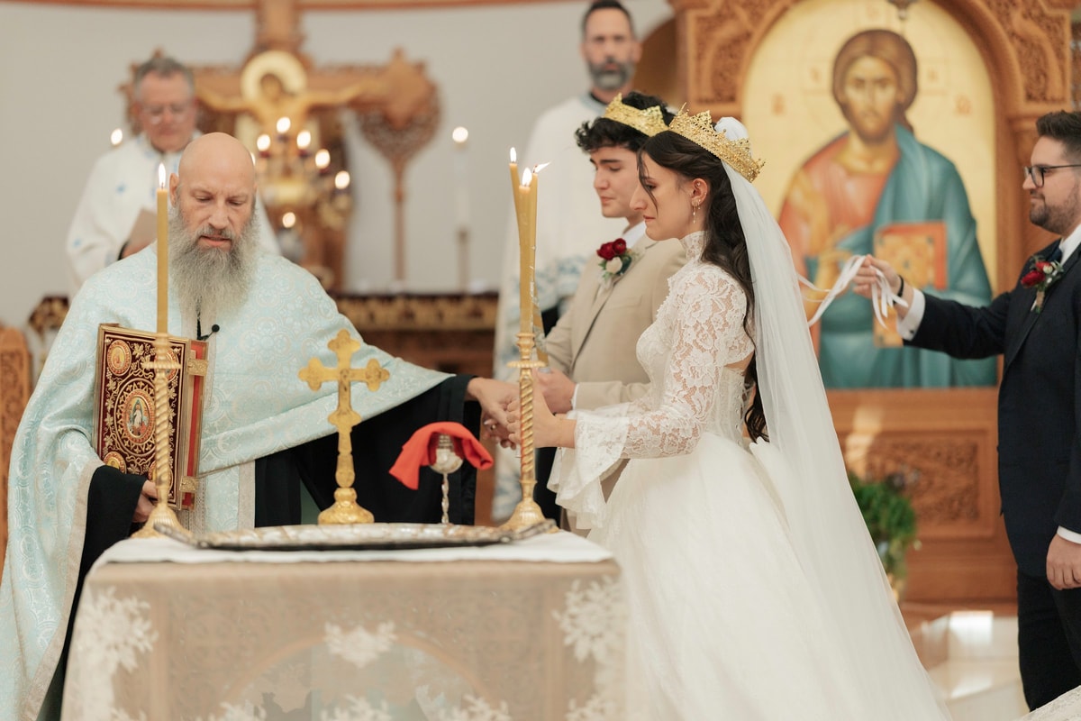 An Orthodox priest carries the Gospel while leading the crowned couple in procession