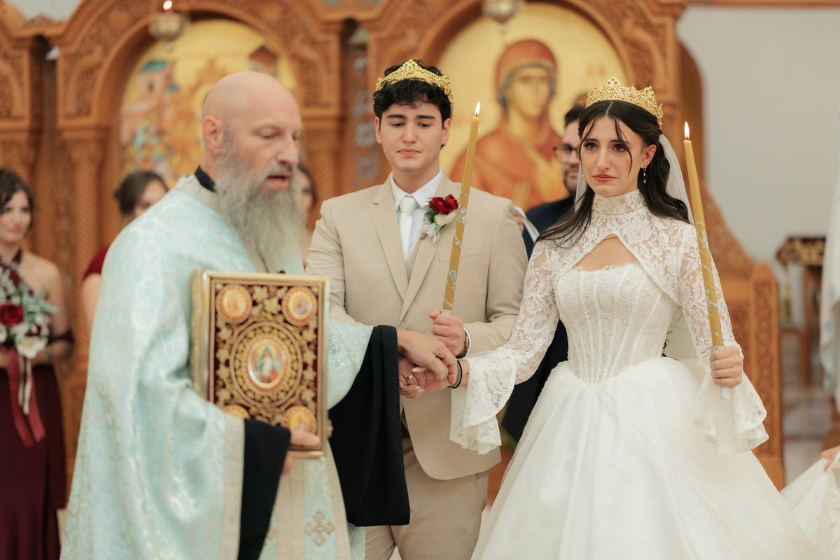 An Orthodox priest carries the Gospel while leading the crowned couple in procession