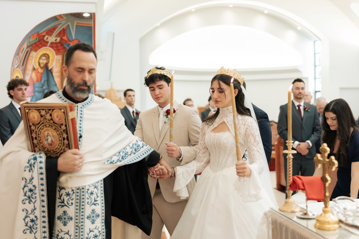 An Orthodox priest carries the Gospel while leading the crowned couple in procession