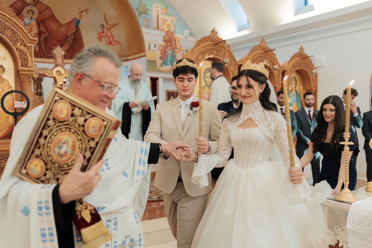 An Orthodox priest carries the Gospel while leading the crowned couple in procession