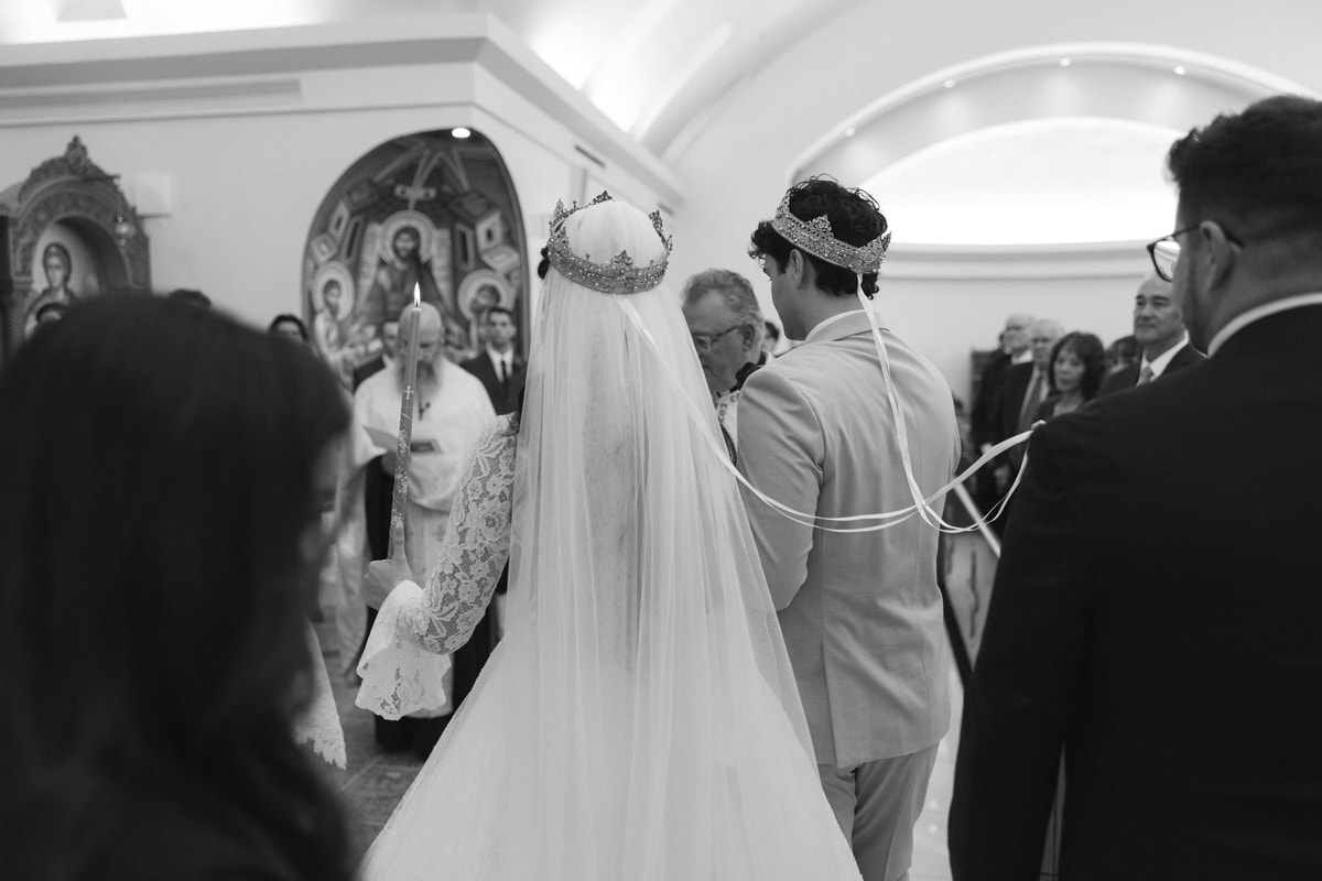 An Orthodox priest carries the Gospel while leading the crowned couple in procession