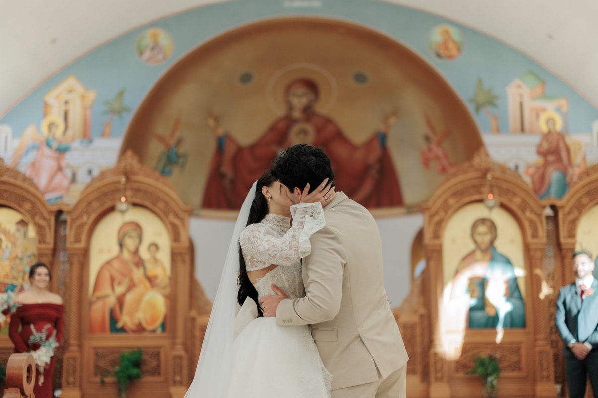 The bride and groom kiss inside an Orthodox church