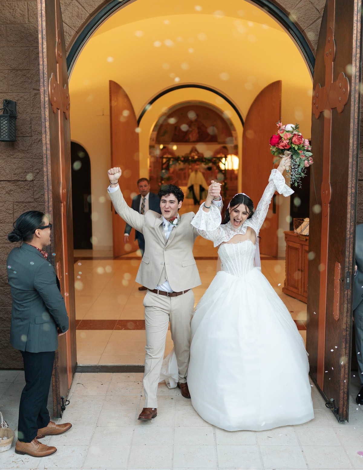 The bride and groom raise their arms as they leave the church