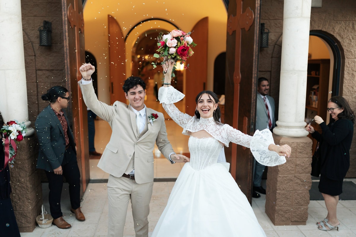 The bride and groom celebrate outside the church with arms raised