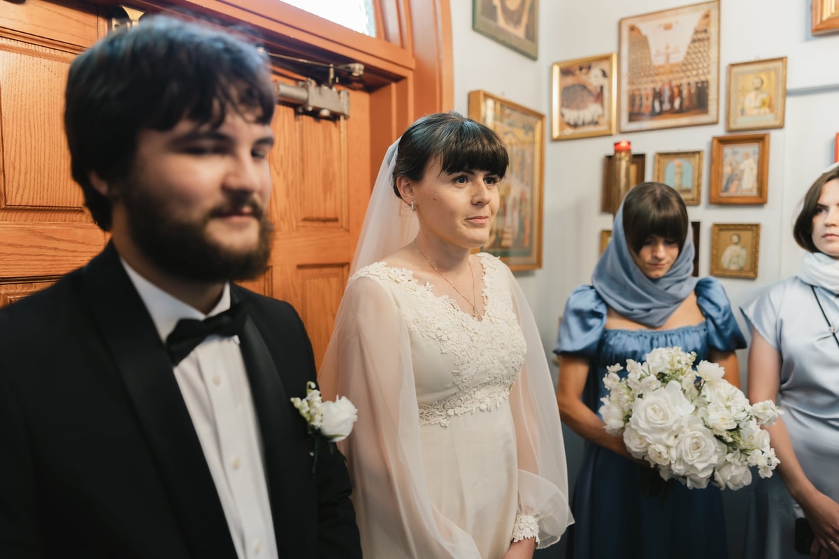 The bride and groom stand at the church entrance before the clergy