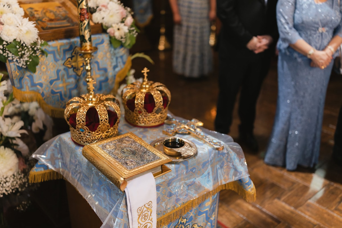 Ornate Orthodox wedding crowns, rings, and the Gospel book on a blue-covered table