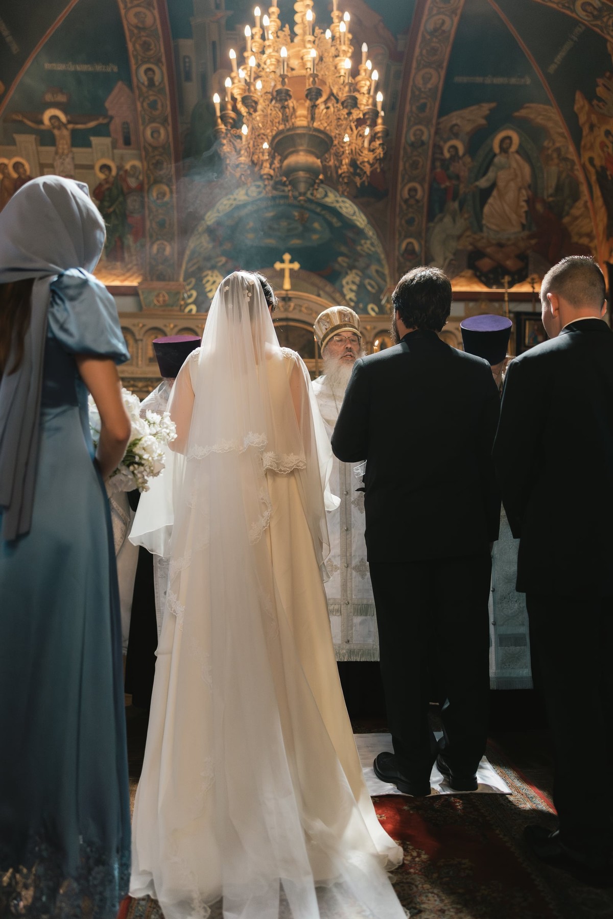 A bride and groom stand before the iconostasis with Orthodox clergy