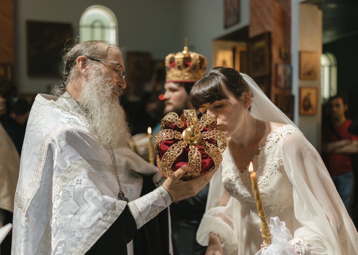 A bride bows to kiss an ornate Orthodox wedding crown