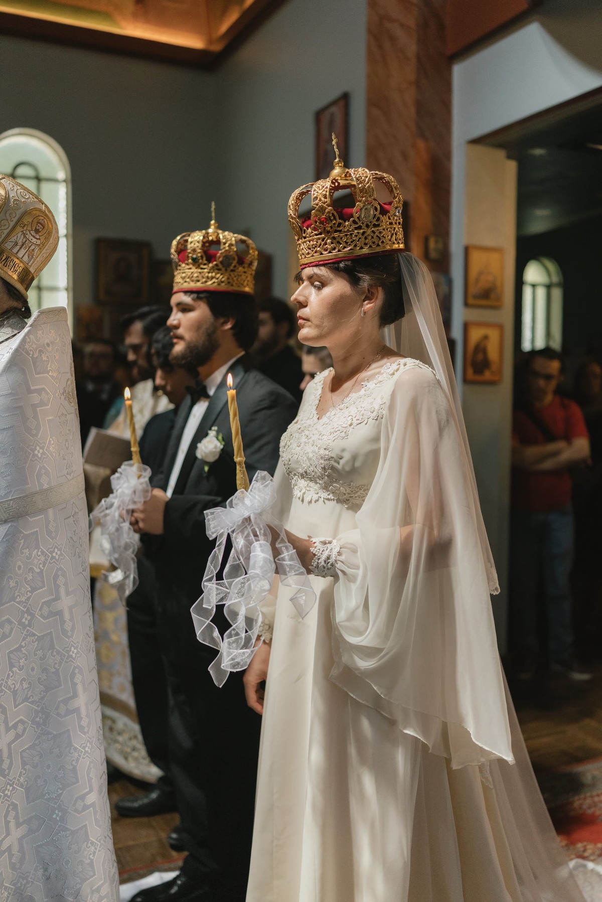 The crowned couple holds candles during the marriage service