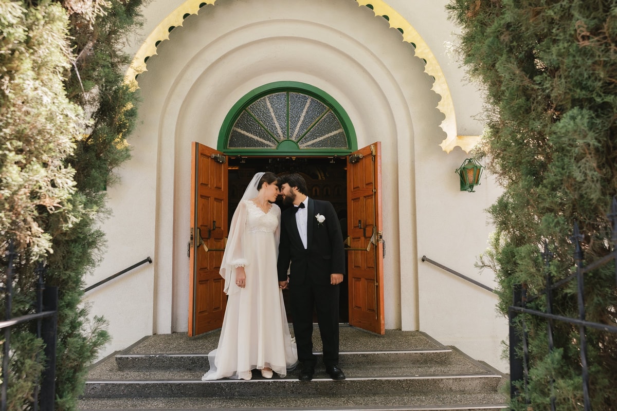 A bride and groom kiss in an Orthodox church doorway