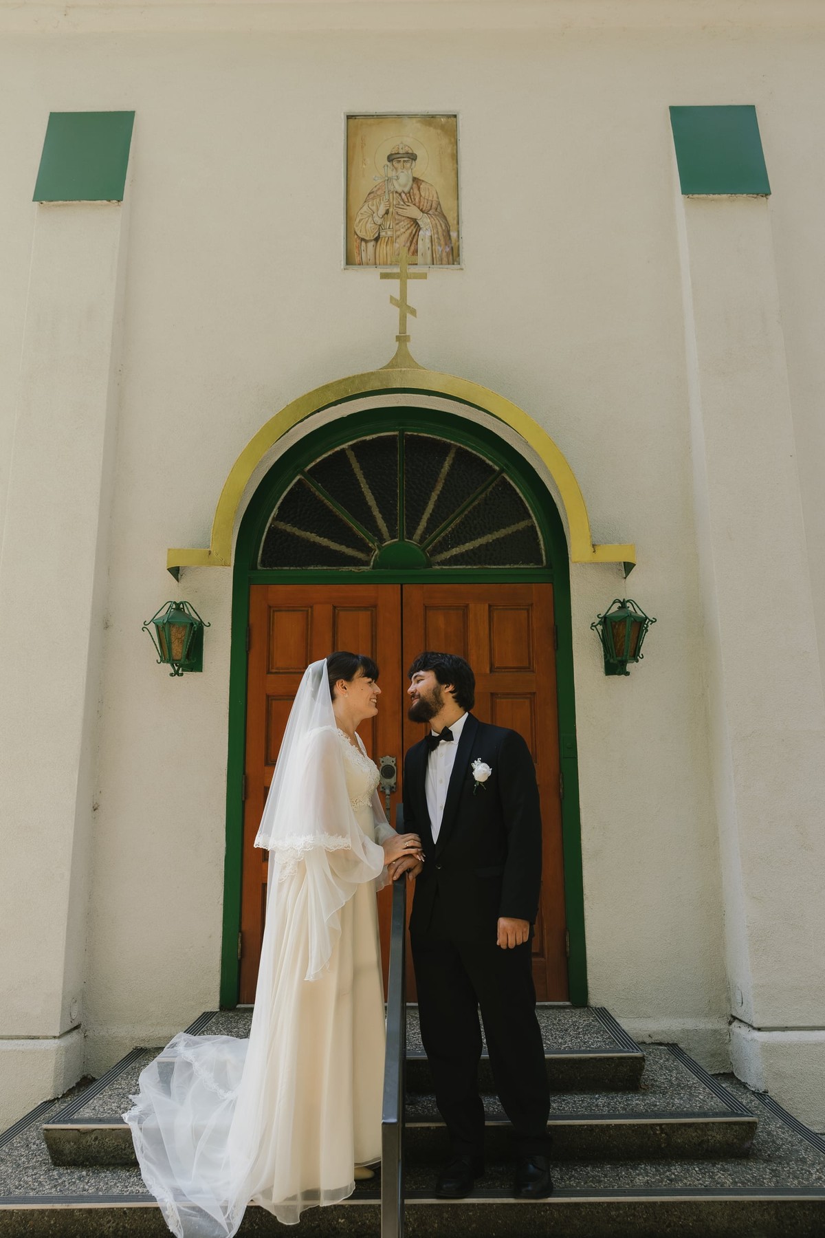A bride and groom stand beneath an arched church entrance