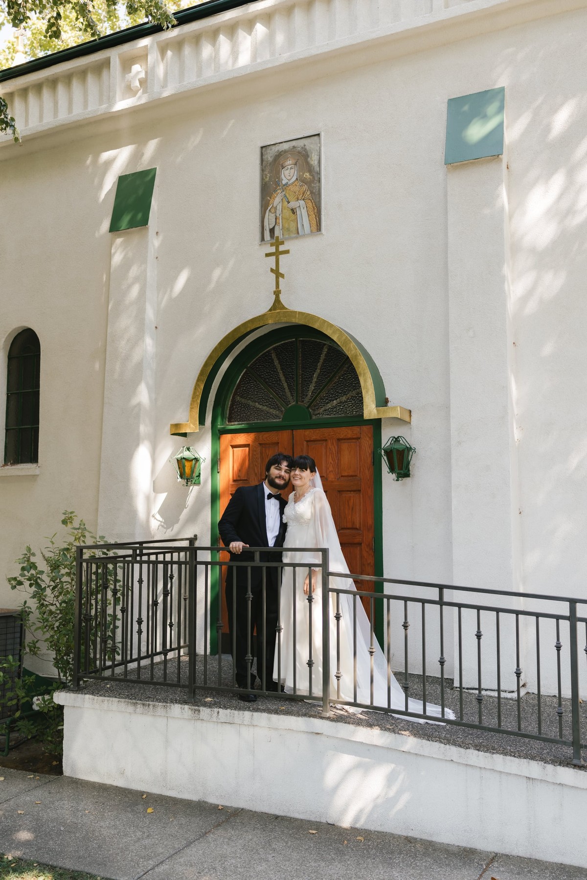 The couple stands on church steps beneath green doors