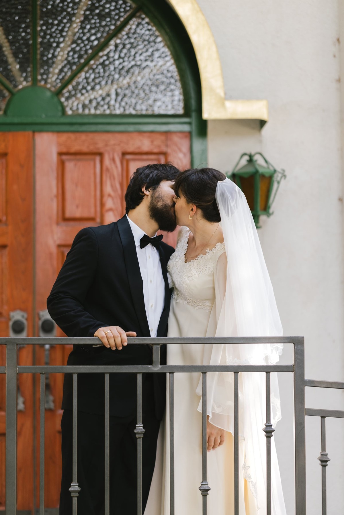 A bride and groom kiss beside a church railing