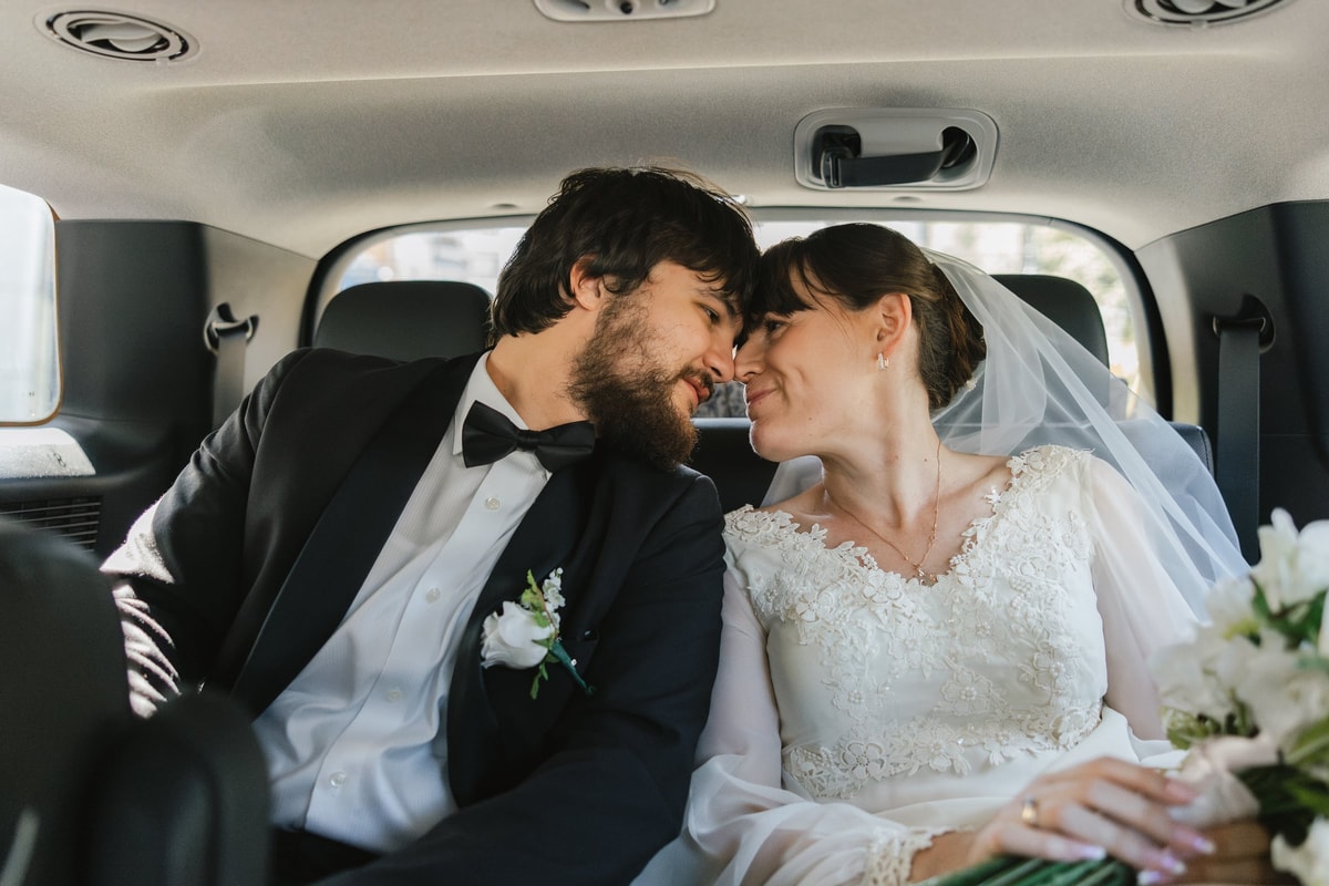 The bride and groom kiss in the back seat of a car