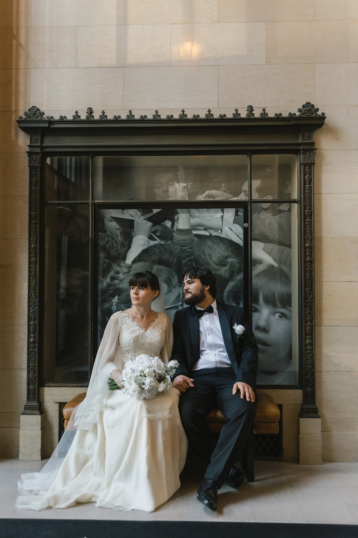 The bride and groom sit together for a portrait by a stone building
