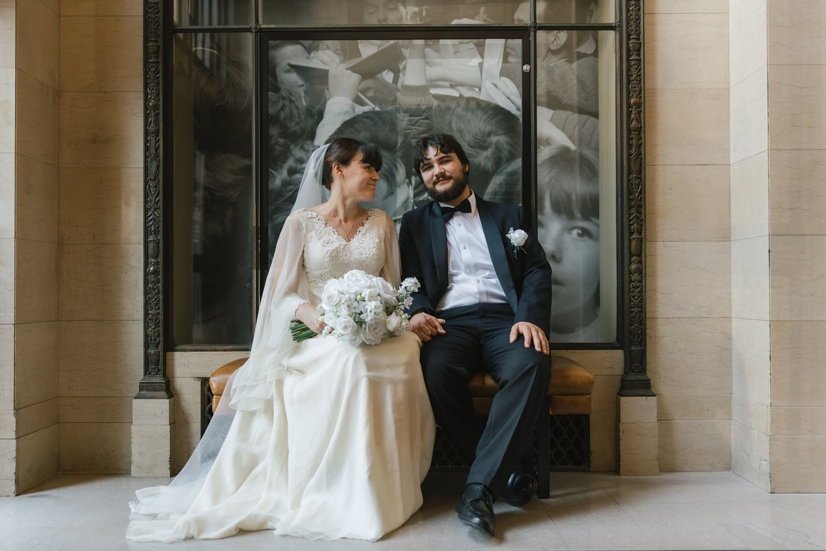 The bride and groom sit together for a portrait by a stone building