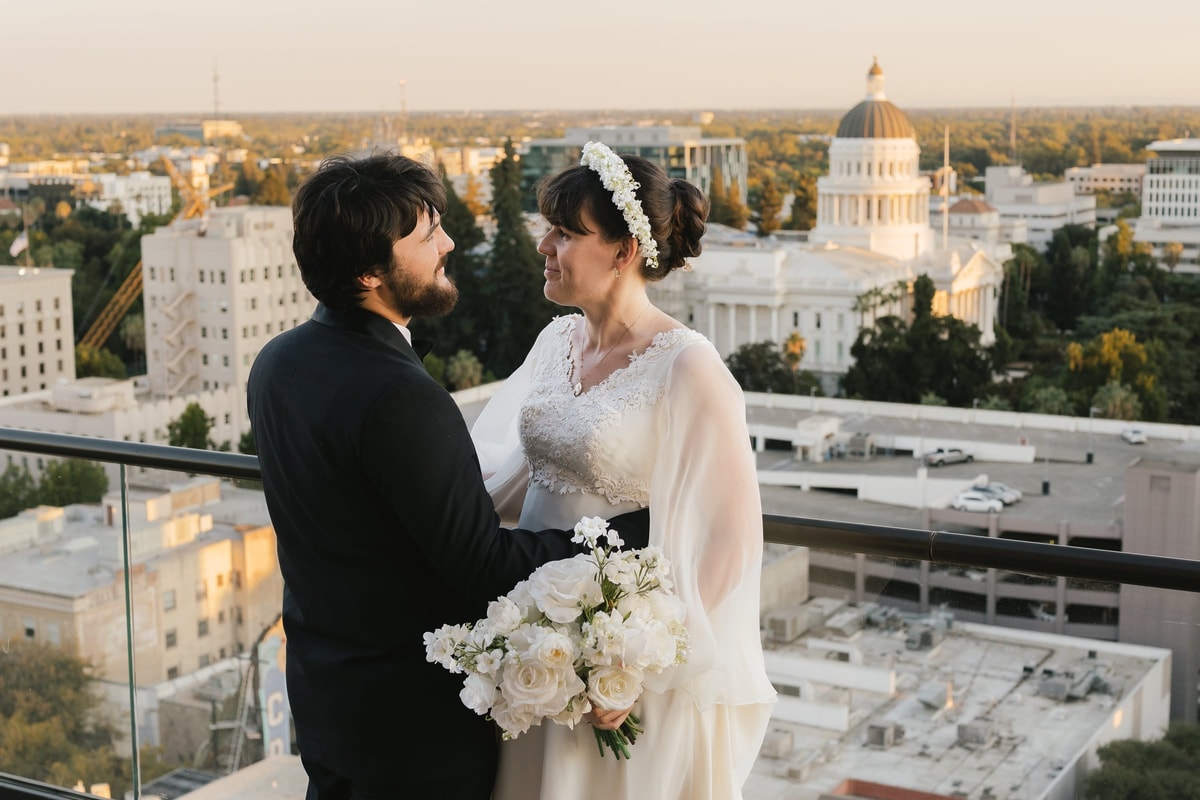 A bride and groom embrace on a rooftop above the city
