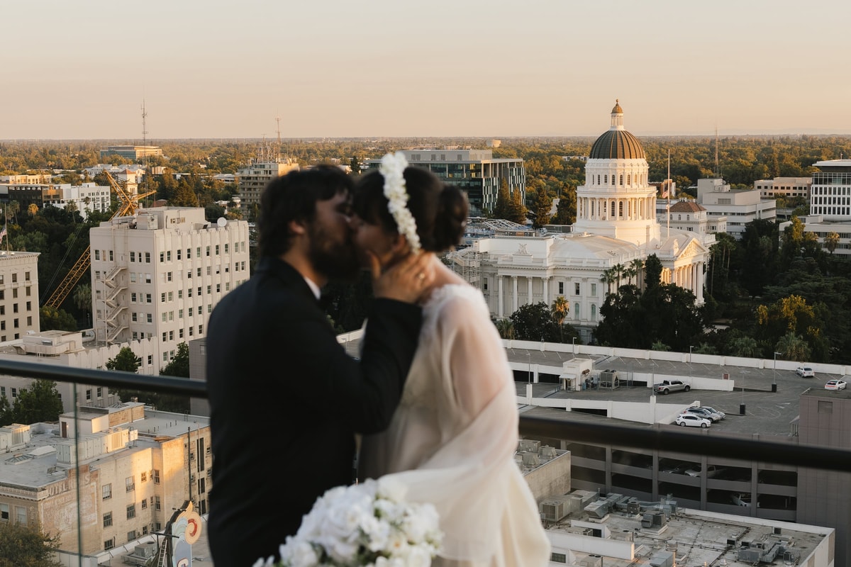 A bride and groom embrace on a rooftop above the city