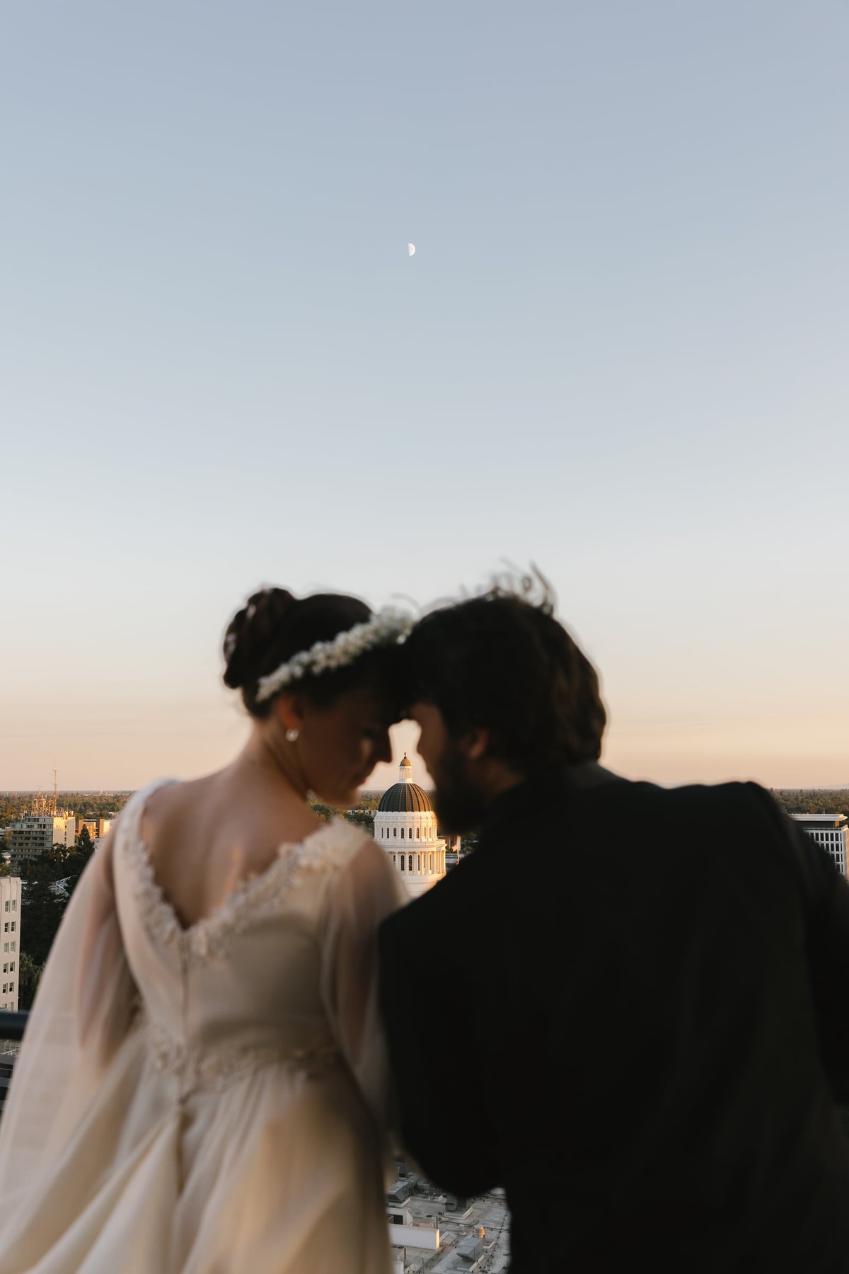 The bride and groom lean together at sunset above the city