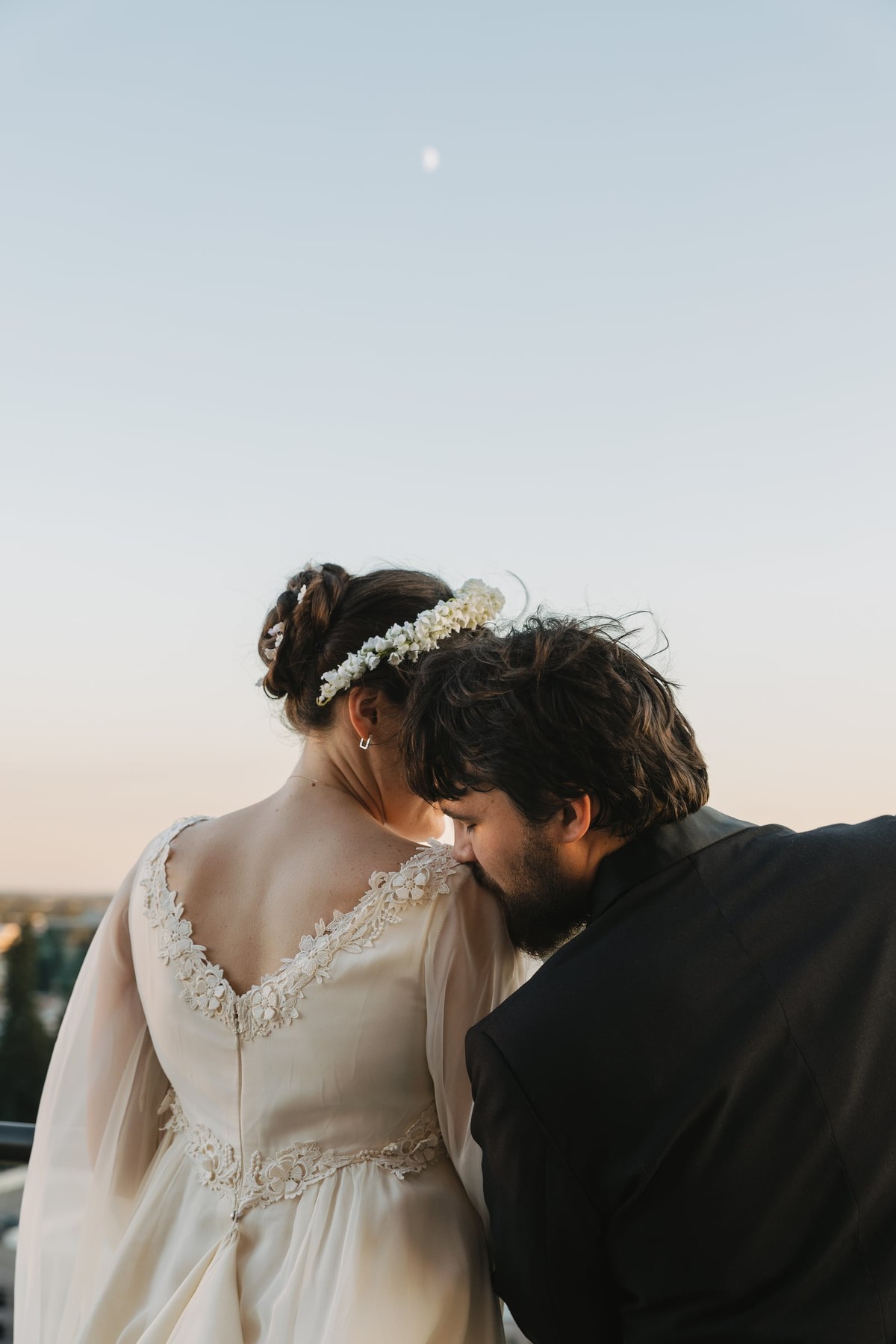 The groom rests his head against the bride on the rooftop