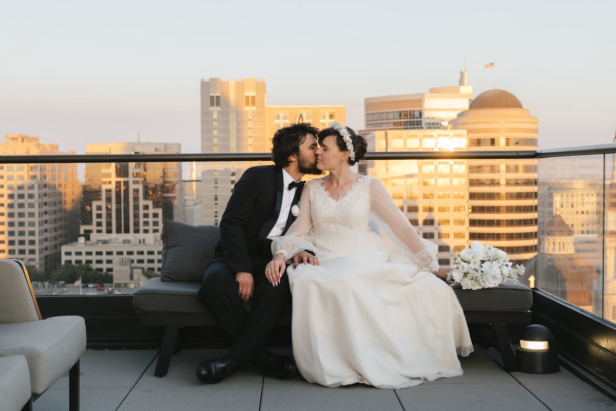 The bride and groom kiss while seated on the rooftop terrace