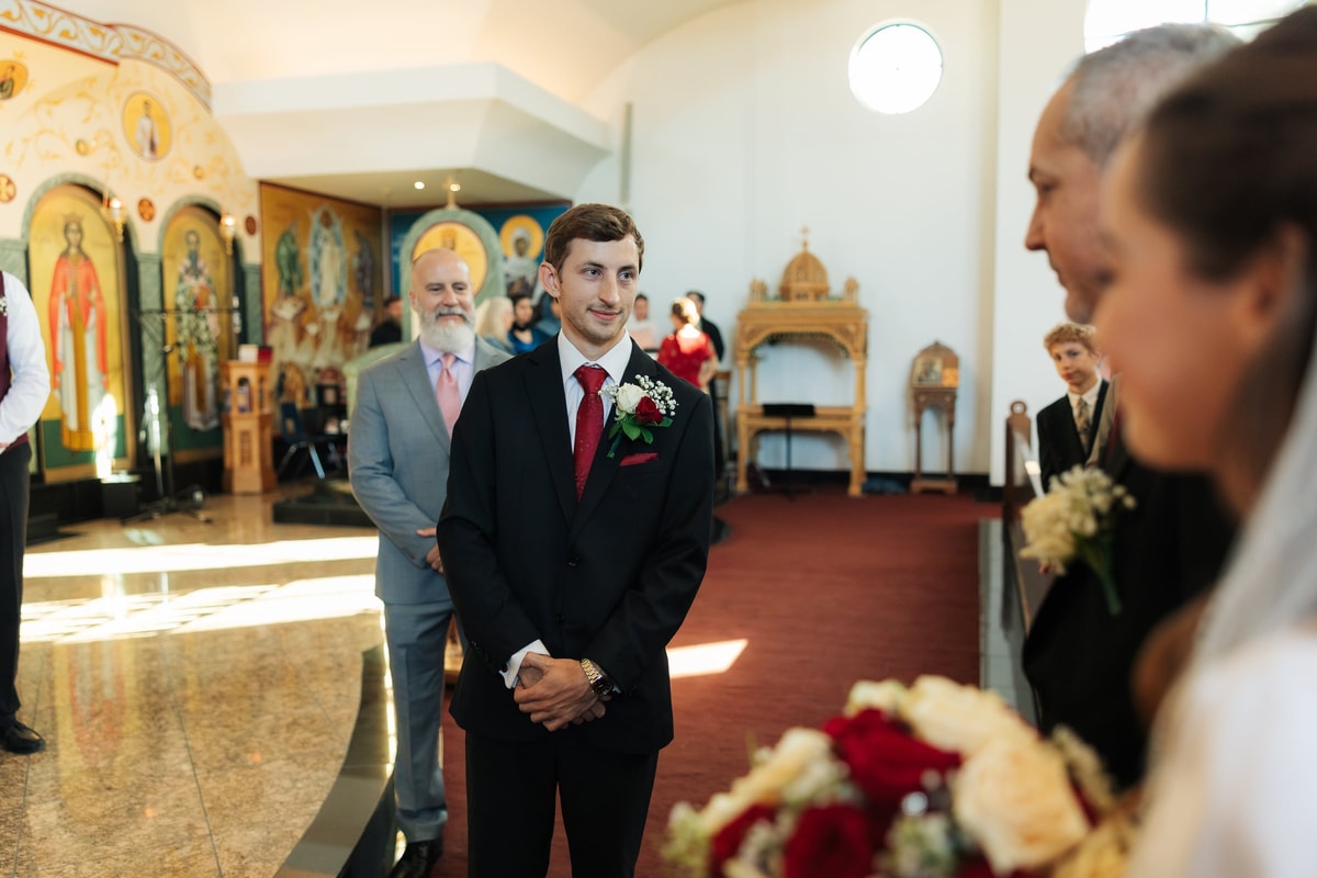 The groom watches the bride approach the altar