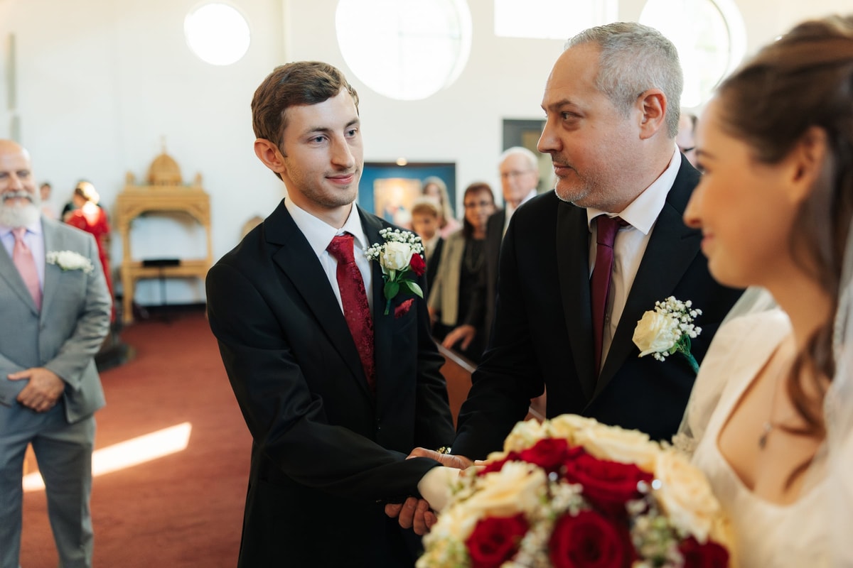 The bride's escort greets the groom at the front of the church