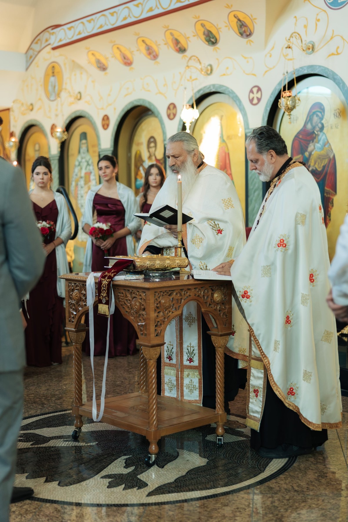 The bride and groom stand with the clergy before the iconostasis