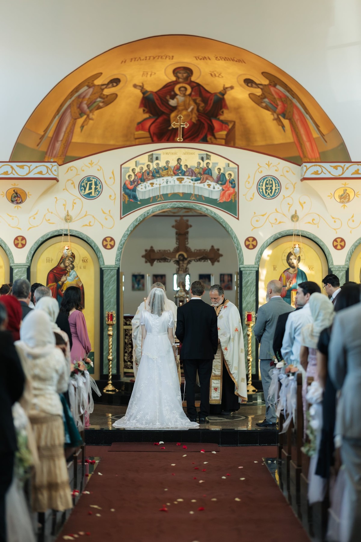 The bride and groom stand with the clergy before the iconostasis