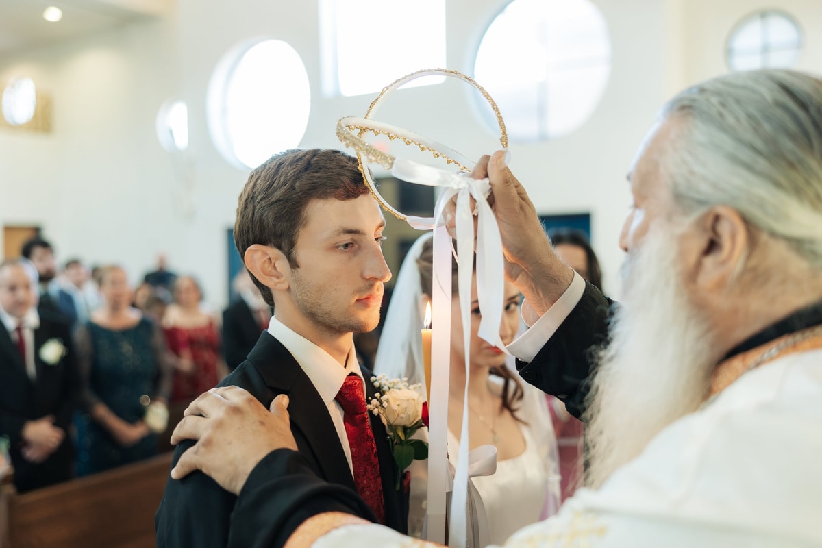 A priest holds a wedding crown above the groom