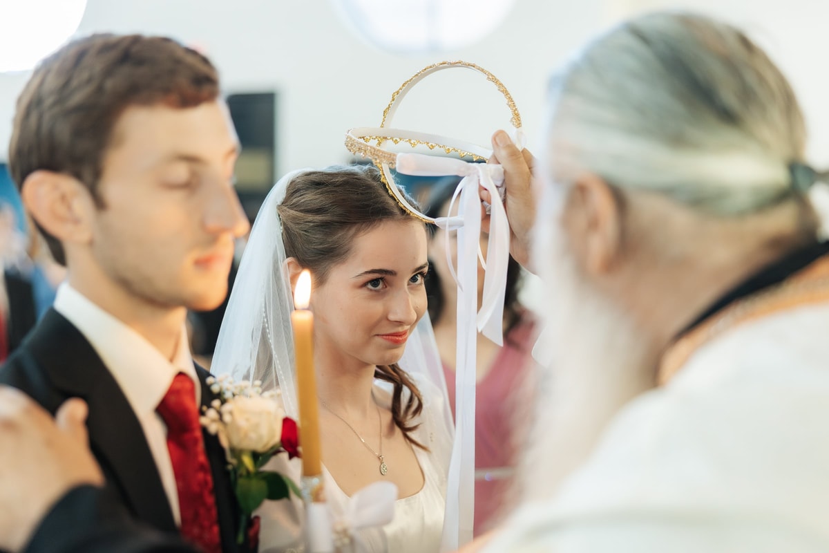 A priest holds a wedding crown above the bride