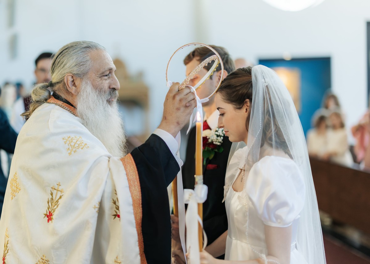 A priest holds a wedding crown above the bride