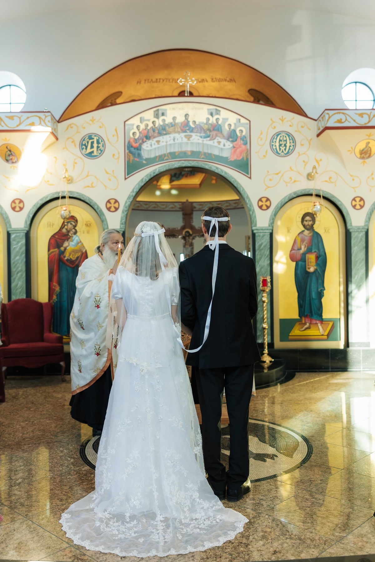 The bride and groom stand crowned before the iconostasis