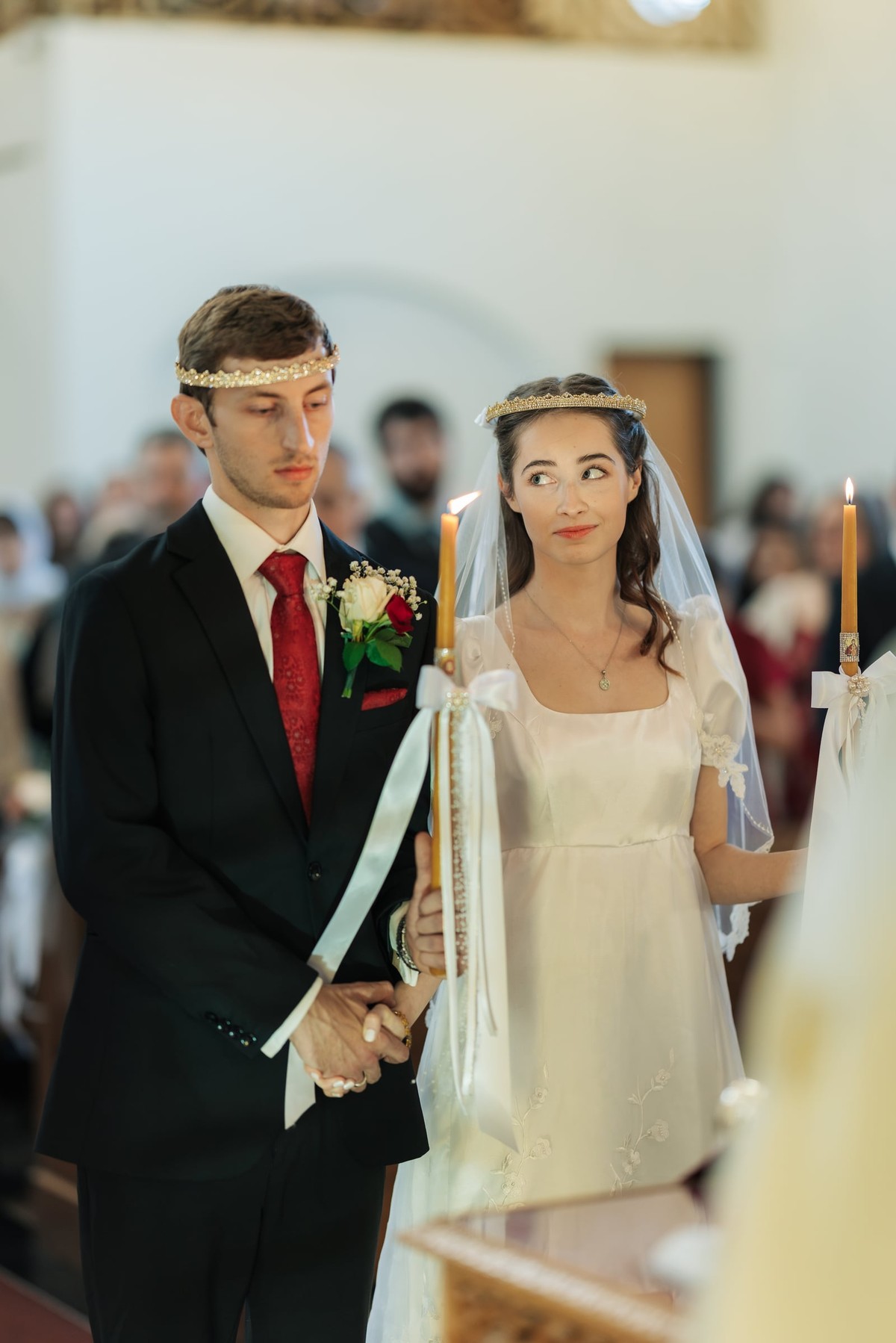 The crowned couple stands together holding candles