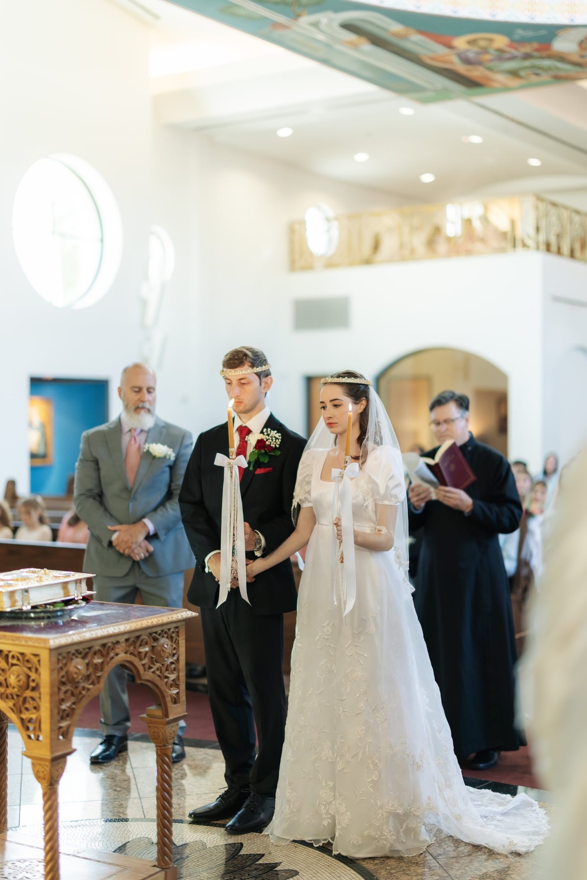 The bride and groom stand crowned beside their sponsor