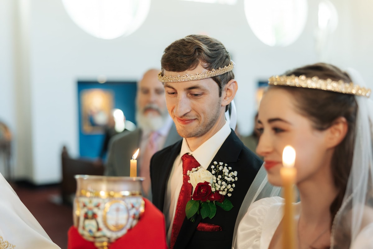 The crowned bride and groom stand together holding wedding candles