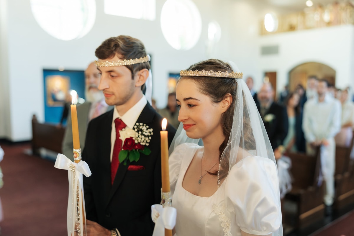 The crowned bride and groom stand together holding wedding candles